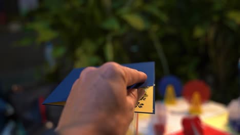 a hand opens a pop-up greeting card of a ferris wheel on a thai street at night