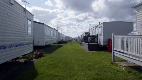 outside-shot-of-static-caravans-on-both-sides,-in-a-caravan-park-with-sun-coming-out-from-behind-the-clouds