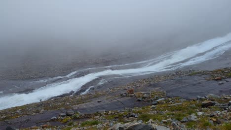 Pan-over-fast-flowing-glacier-river-in-remote,-stony-and-foggy-environment