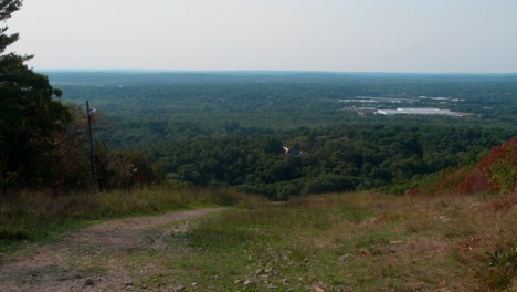 A-tilt-reveal-of-a-colorful-mountain-seen-from-the-summit-displaying-dense-forest-in-the-distance