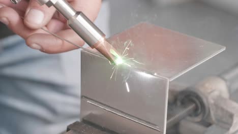 professional showcasing laser welding device, connecting two rectangular pieces of sheet metal while sparks fly using filling rod