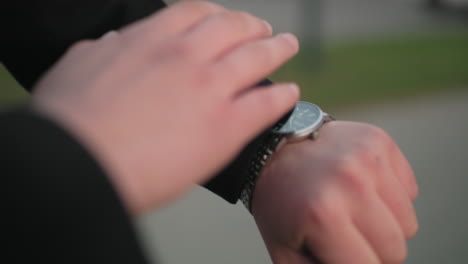 close up of hand opening suit cloth to check time, blurred background with greenery and unclear object, focus on hand gesture, time management, and professional style