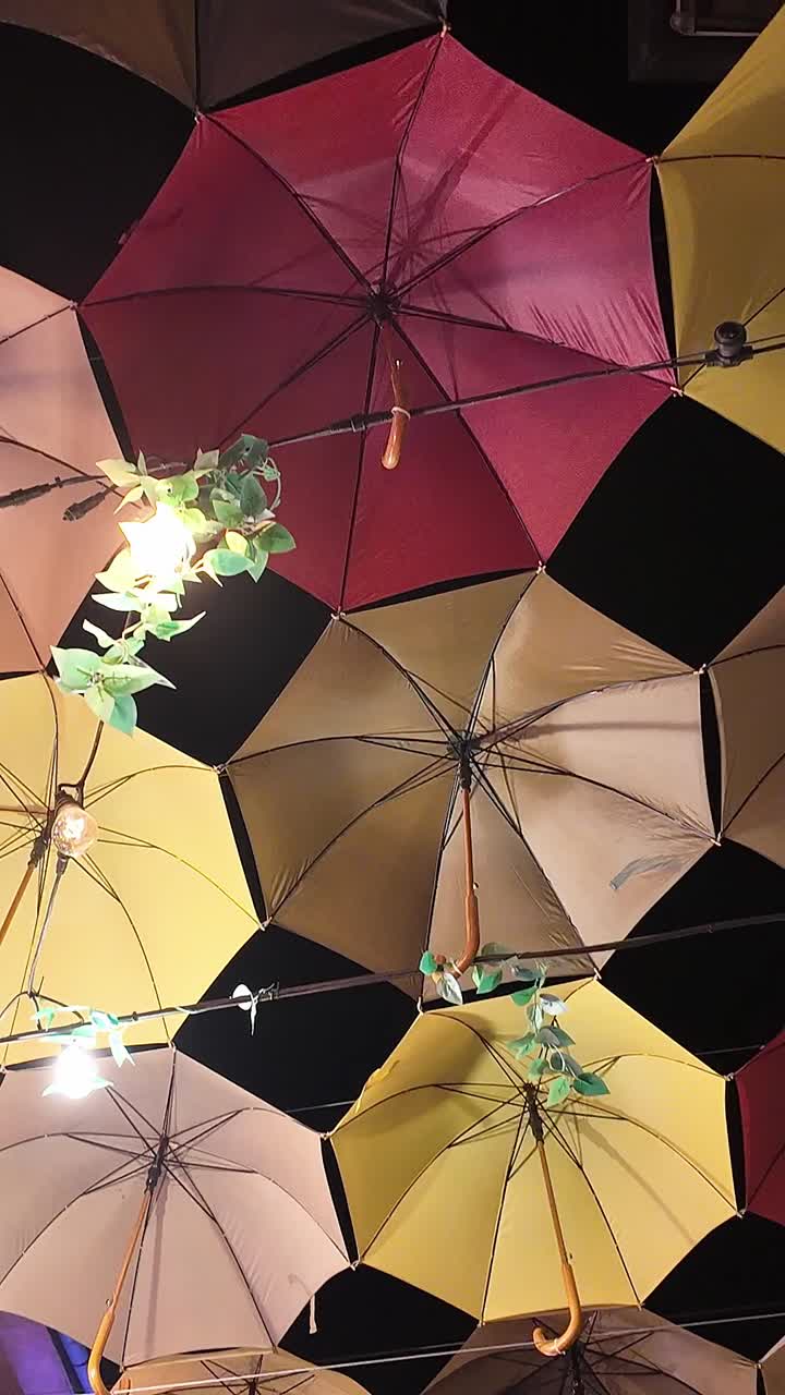 Multi-colourful umbrellas hang from wires above lit street at night