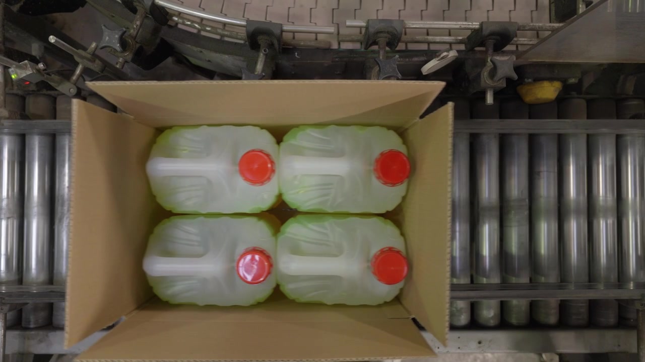 Draufsicht auf vier verschlossene Chemikalienkanister, ordentlich verpackt in einem offenen Karton auf einem Rollenförderband