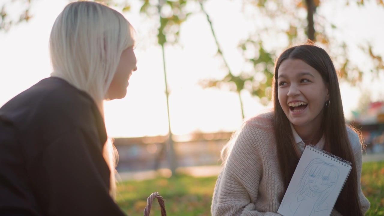 Ragazza adolescente che mostra il suo disegno del quaderno da disegno a un'amica al parco.