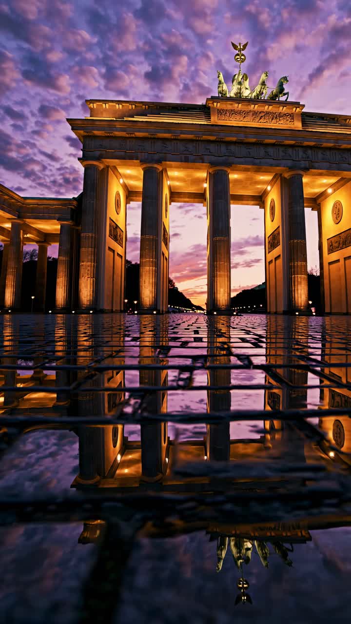 Toma a contrapicado de la Puerta de Brandeburgo al atardecer, capturando su reflejo en el pavimento mojado