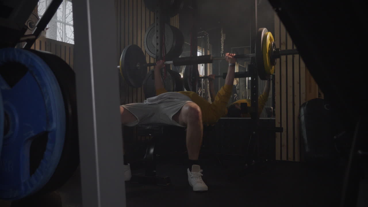 Static view of man lying on a bench exercising with a barbell. Indoor