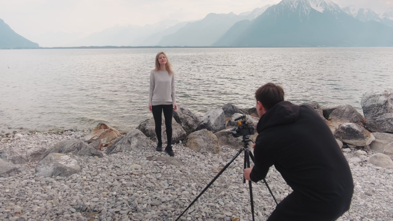 Male photographer posing a blonde model with lake at beach during the day, gimbal shot