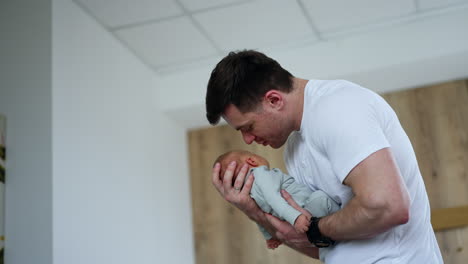 happy mid-aged caucasian man swaying his little baby. loving new-made dad caressing newborn son. low angle view.