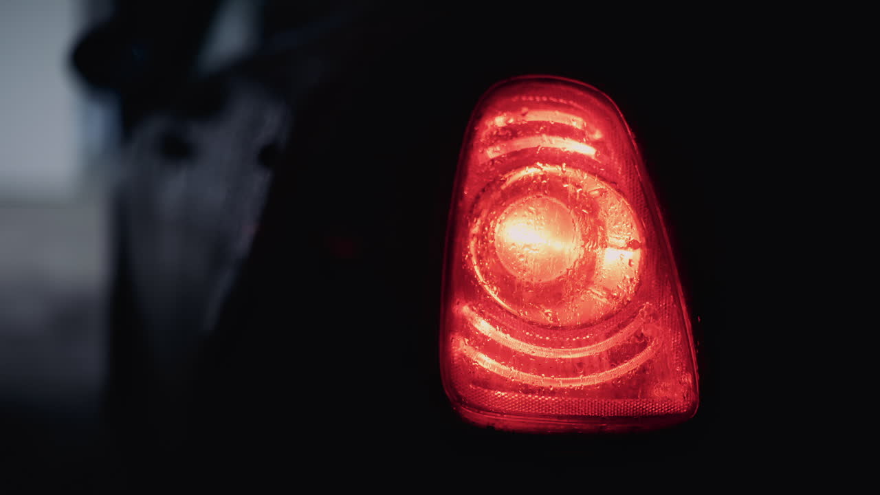 Close up shot of a glowing red car taillight covered in raindrops at night