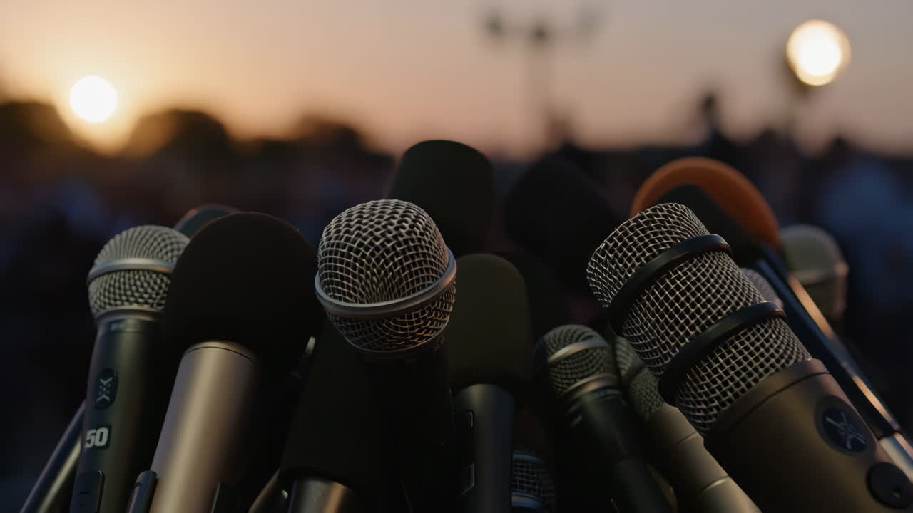 A close-up shot of multiple microphones at a press conference with a sunset in the background