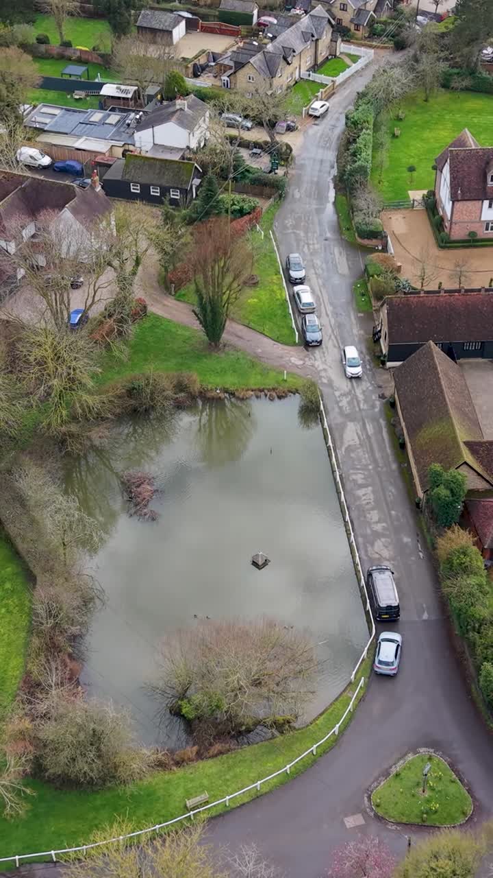 Chapmore End vertical drone shot rises backward over the main road, duck pond and village houses in rural Hertfordshire, England, revealing countryside streetscape and calm suburban life