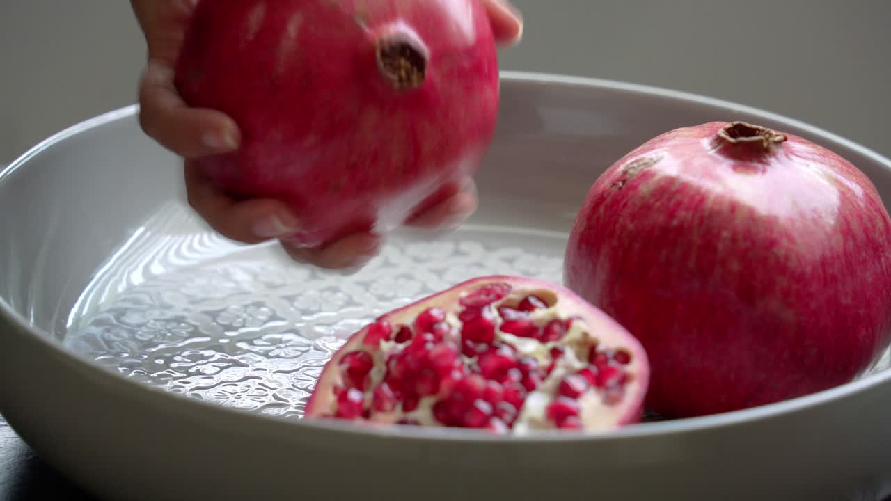 Holder et skåret granatæble med lyse røde kerner på en tallerken. Med sunde antioxidanter og hjertebeskyttende egenskaber.
