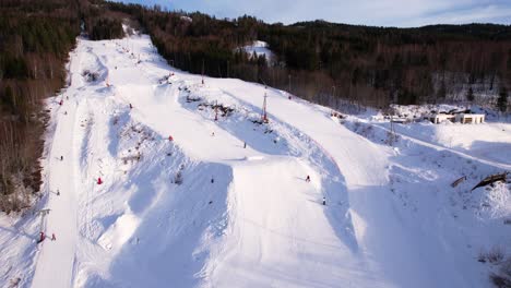 Cinematic-drone-view-of-skiers-gliding-down-a-beautiful-ski-slope-in-Vikersund,-Norway-in-a-beautiful-sunny-winter-day