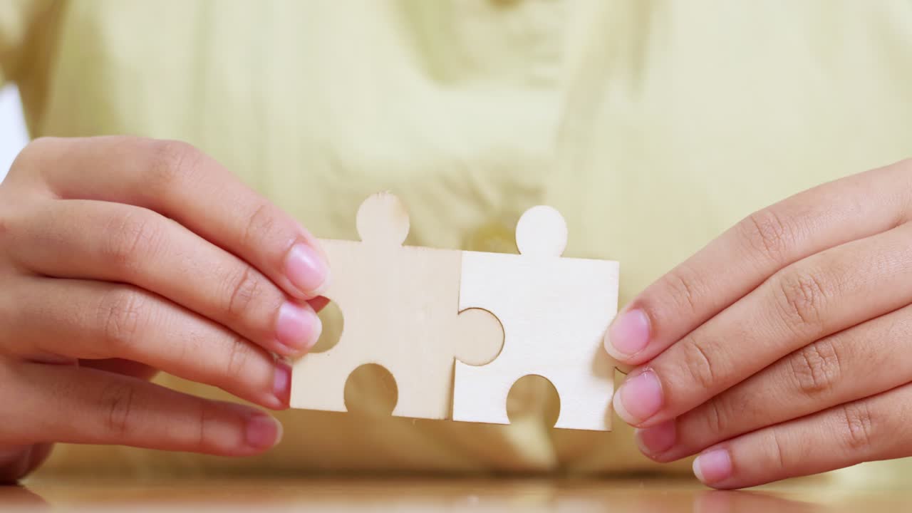 Two hands connect puzzle pieces symbolizing teamwork and collaboration in a home office setting