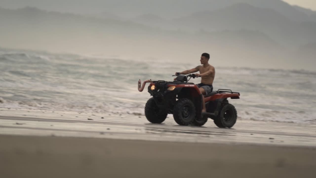 Un uomo guida un quad ATV attraverso le ampie rive sabbiose di una spiaggia a Santa Teresa, Costa Rica