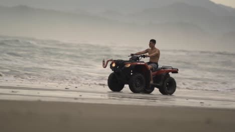 a man rides an atv quad bike across the wide, sandy shores of a beach in santa teresa, costa rica