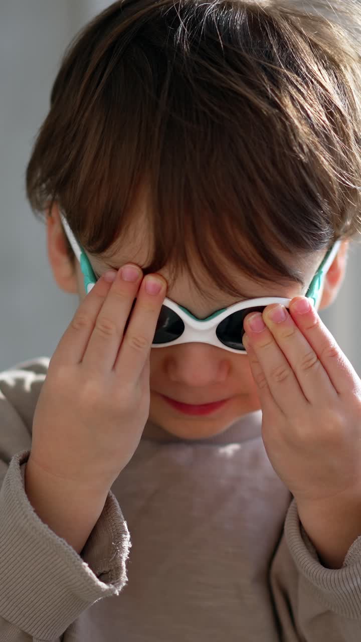 Adorabile bambino con maglione grigio e occhiali da sole. Ritratto ravvicinato del bambino all'interno. Video verticale