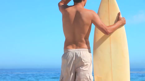 good looking man with his surfboard looking out to sea