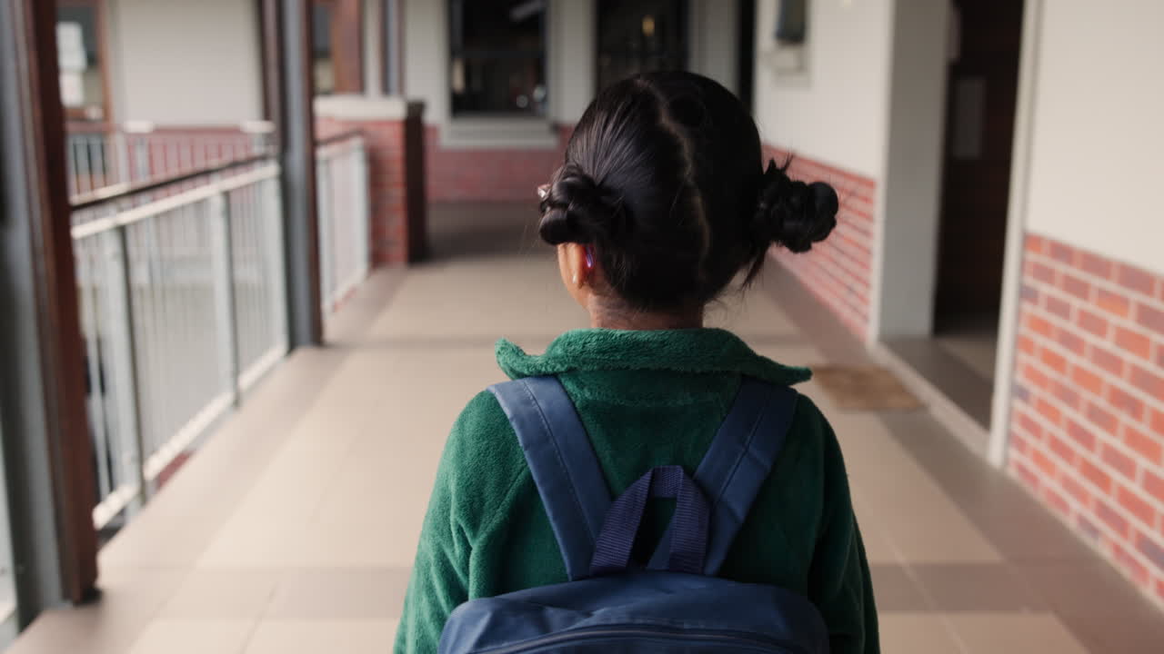 A girl walking down a school hallway with her backpack on