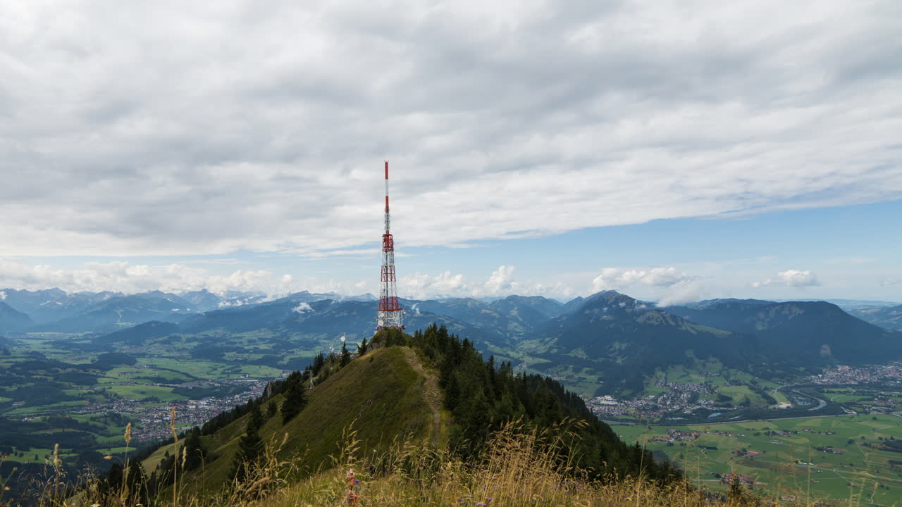 Time-lapse shot of clouds in front of a radio mast on the Grünten (mountain) in the Allgäu Alps in Bavaria, Germany. In the foreground, the grass moves in the wind.