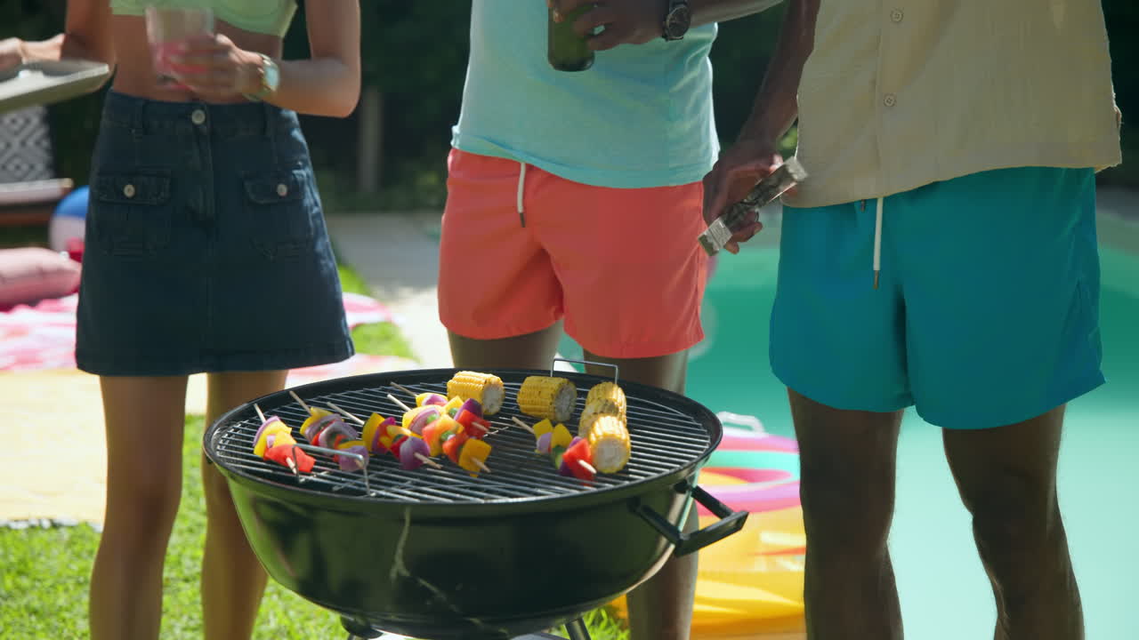 Diverse friends enjoying drinks and laughter outdoors by pool on sunny day