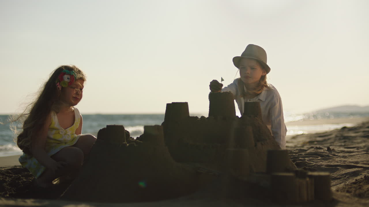 dos chicas construyendo un castillo de arena en la playa al atardecer