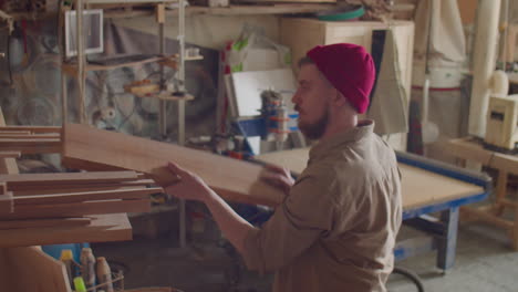 woodworker taking plank from shelf in carpentry workshop