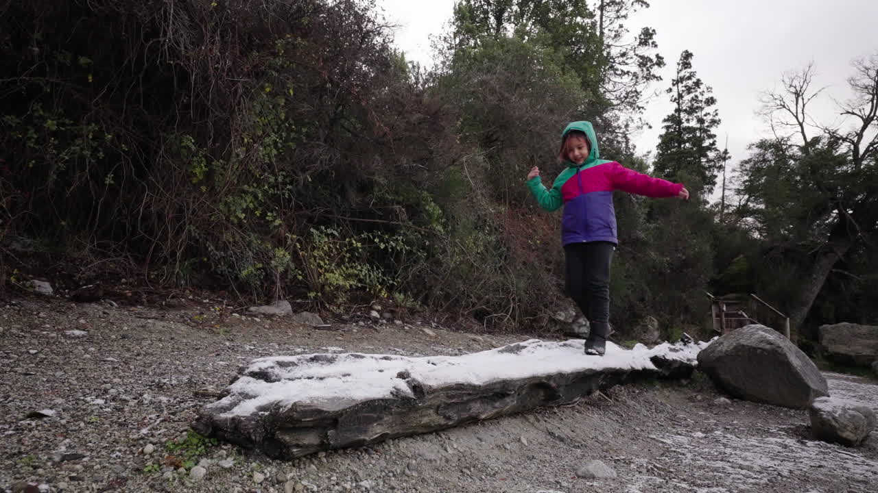 Happy child balancing on icy tree trunk, playful winter day in Argentine forest