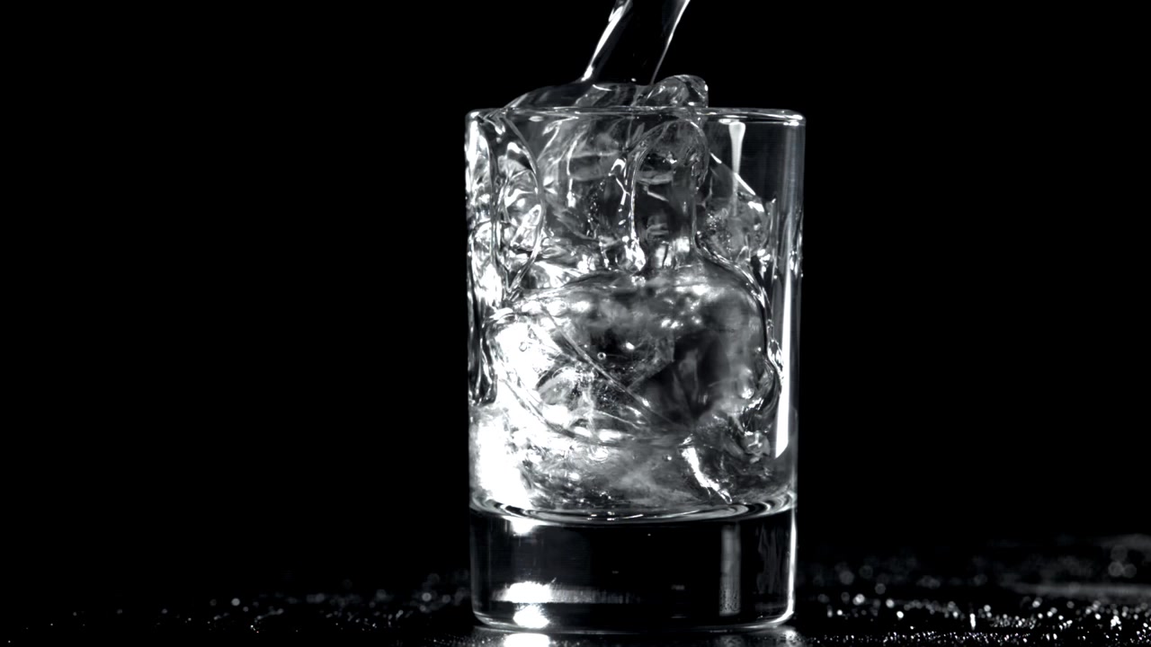 Vand hældes i glas med isterninger på sort baggrund