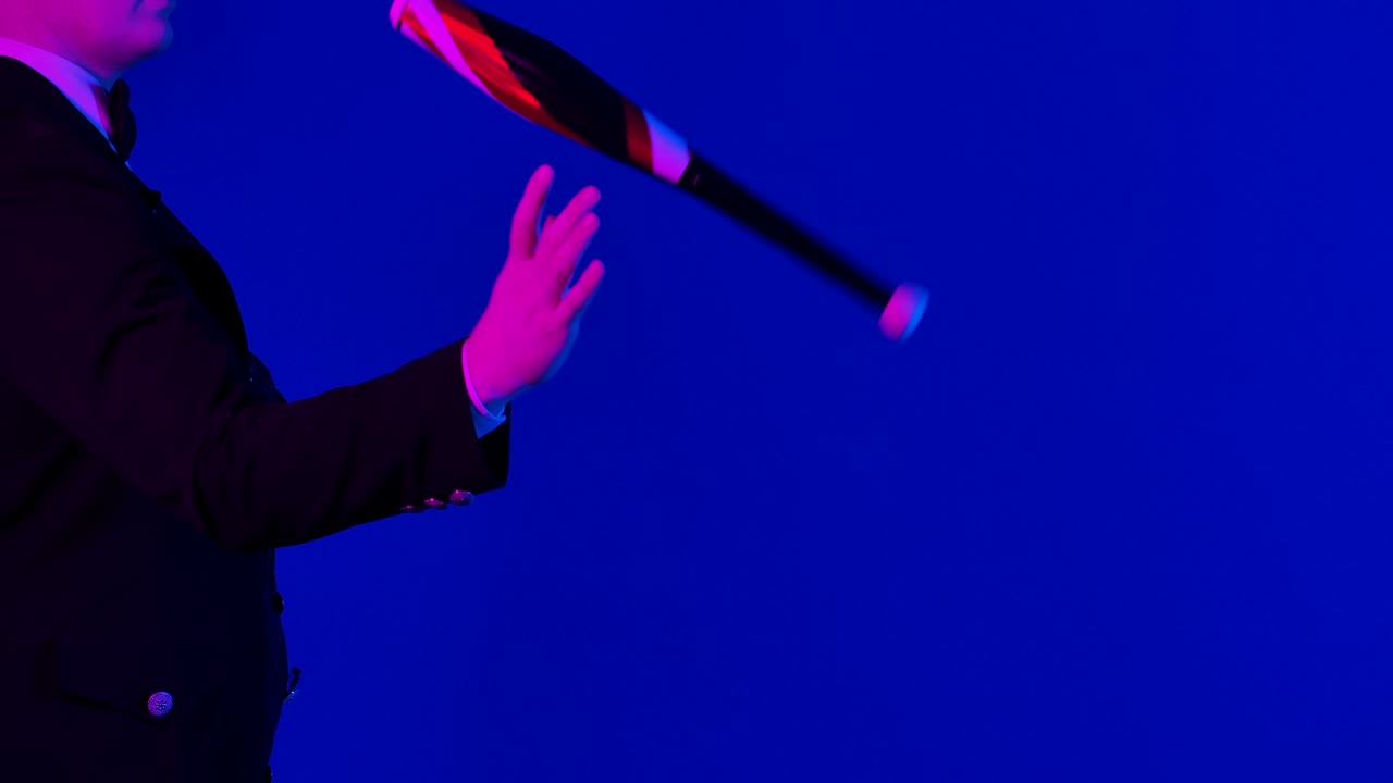 Side view of a man rotating a pin for juggling. A professional circus actor practices his skill in a dark studio. Blue screen, chroma key. Close up. Slow motion