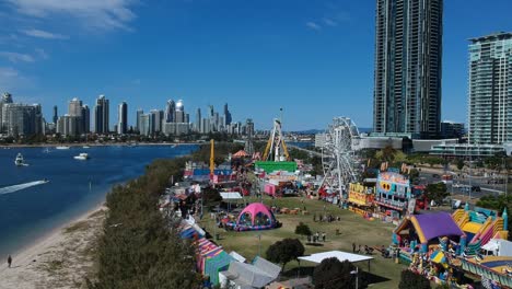 aerial view of a colourful carnival situated by the sea with a city skyline in the background