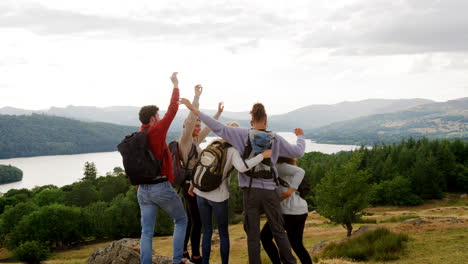 un grupo multiétnico de cinco felices amigos adultos jóvenes aplauden con los brazos en el aire, saludan y se abrazan en la cumbre durante una caminata por la montaña