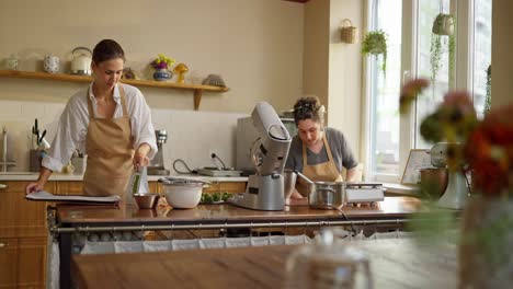 two female bakers working together in a bakery kitchen.