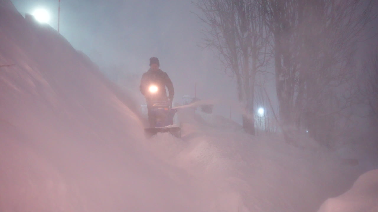 Man using snowblower to clear deep snow during intense blizzard at night