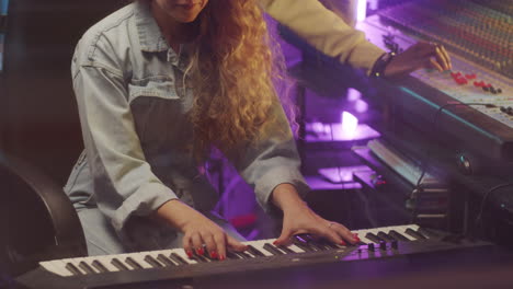 mujer tocando el sintetizador y hombre usando la consola de mezcla en el estudio de grabación