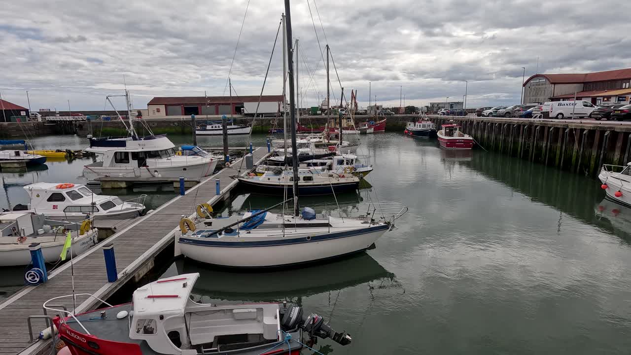 Una fluida panoramica diurna rivela un porto turistico con barche a vela, yacht, banchine e cielo nuvoloso a Fife, in Scozia
