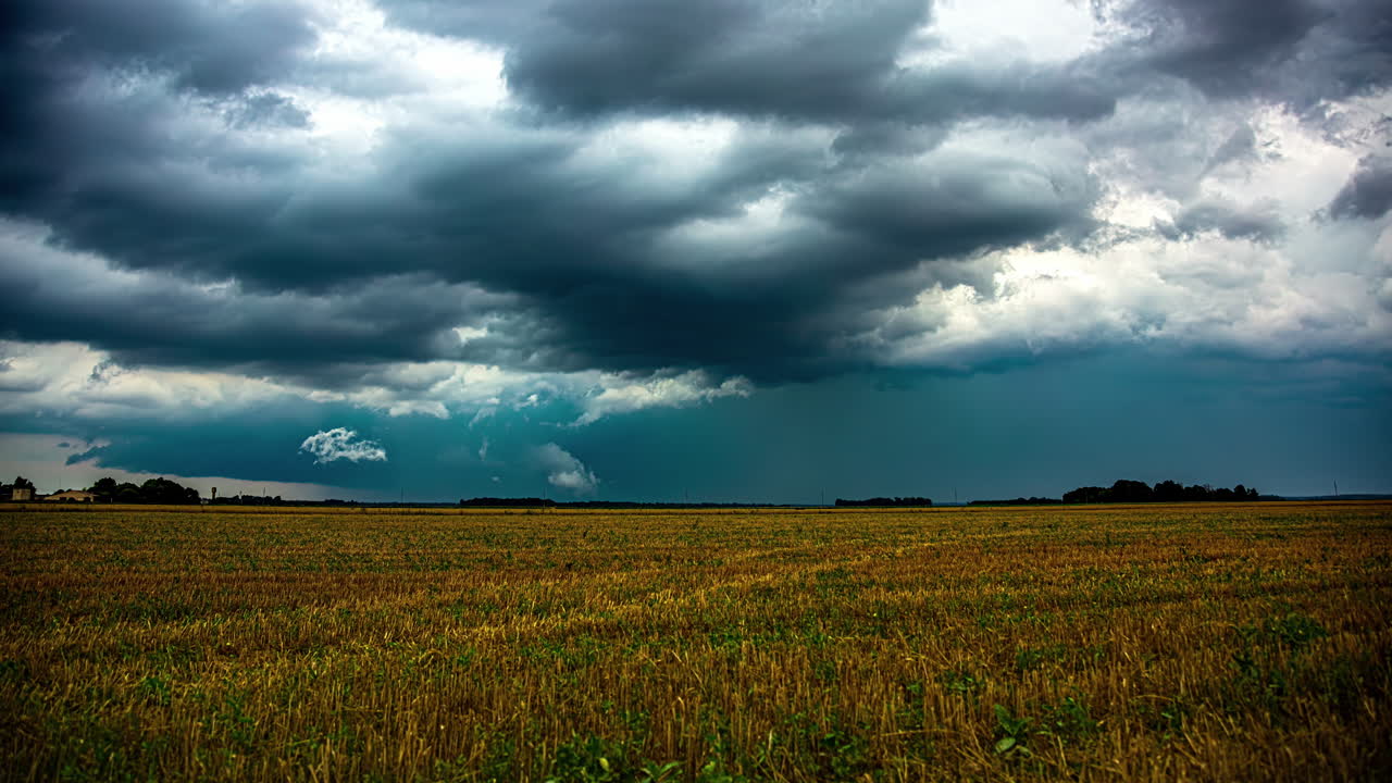 Mächtige dunkle Sturmwolken ziehen über ländlichen Feldern mit arbeitenden Bauern, Zeitrafferaufnahme.