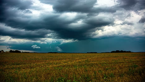 powerful dark storm clouds flowing above rural fields with working farmers, time lapse view