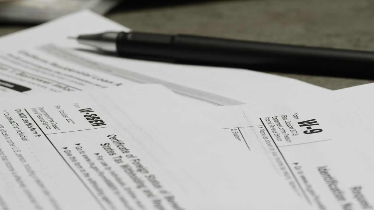 Close-up of Tax Forms W-9 and W-8BEN with a Pen