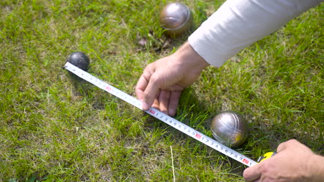 bovenaanzicht van een blanke jonge man die de afstand tussen petanqueballen in het park berekent