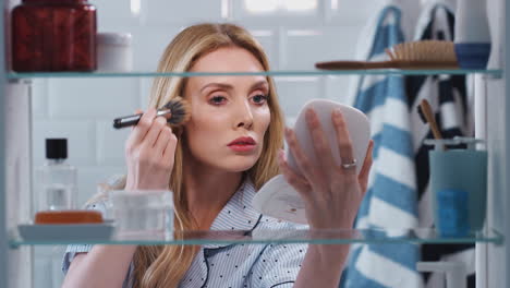 View-Through-Bathroom-Cabinet-Of-Young-Woman-Wearing-Pajamas-Putting-On-Make-Up