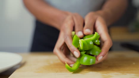 manos de mujer de piel oscura colocando pimientos verdes picados junto al resto de las verduras en un plato