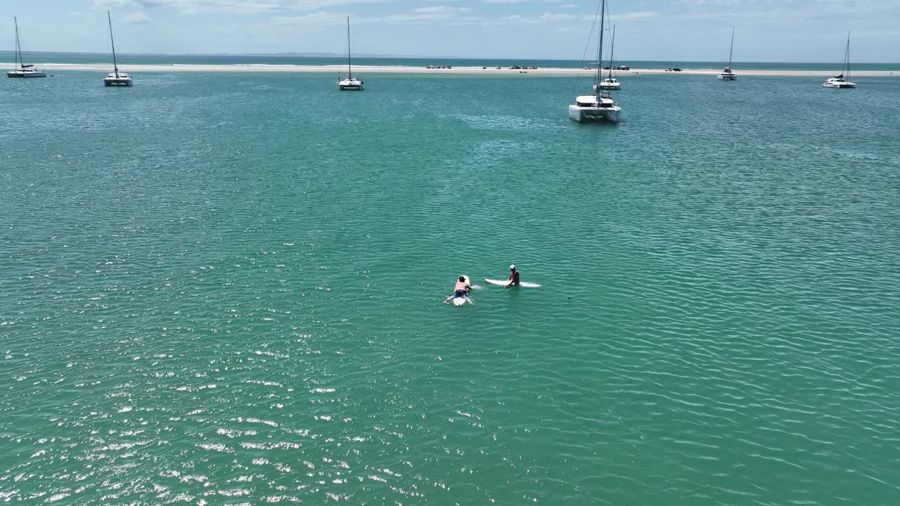 vuelo inverso sobre catamaranes amarrados para revelar a dos hombres en tablas de surf.