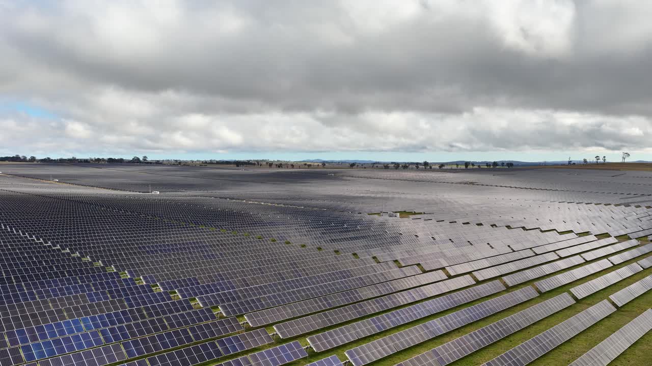 Wide aerial pan across solar panel field under cloudy sky, emphasizing renewable energy infrastructure