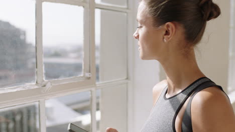 beautiful yoga woman using smartphone texting sharing training practice on social media looking out window planning ahead in wellness studio