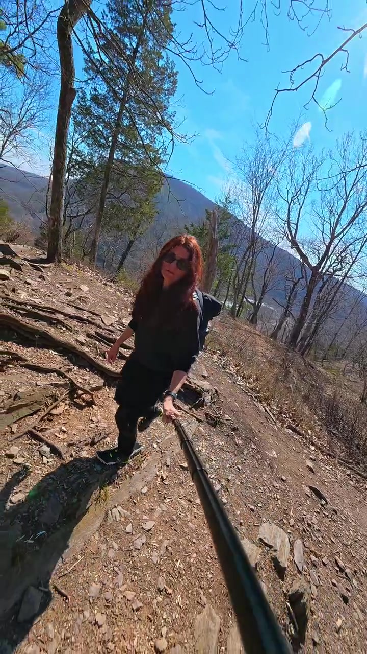 Donna escursionista su sentiero di montagna roccioso con bastone per selfie. Un'escursionista con zaino cammina su sentiero sterrato e roccioso sul Monte Tammany, ripresa con bastone per selfie.