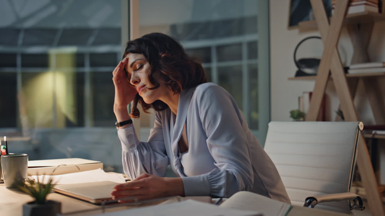 Freelancer oberato di lavoro che finisce un progetto online alla scrivania dell'ufficio a tarda sera, primo piano.
