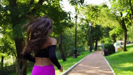 Back-view-of-a-young-woman-in-fuxy-legging-running-in-the-sunny-city-park-exercising-outdoors.-Steadicam-stabilized-shot