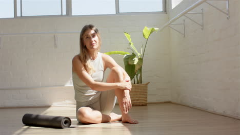 mujer caucásica sentada en el suelo junto a la alfombra de yoga